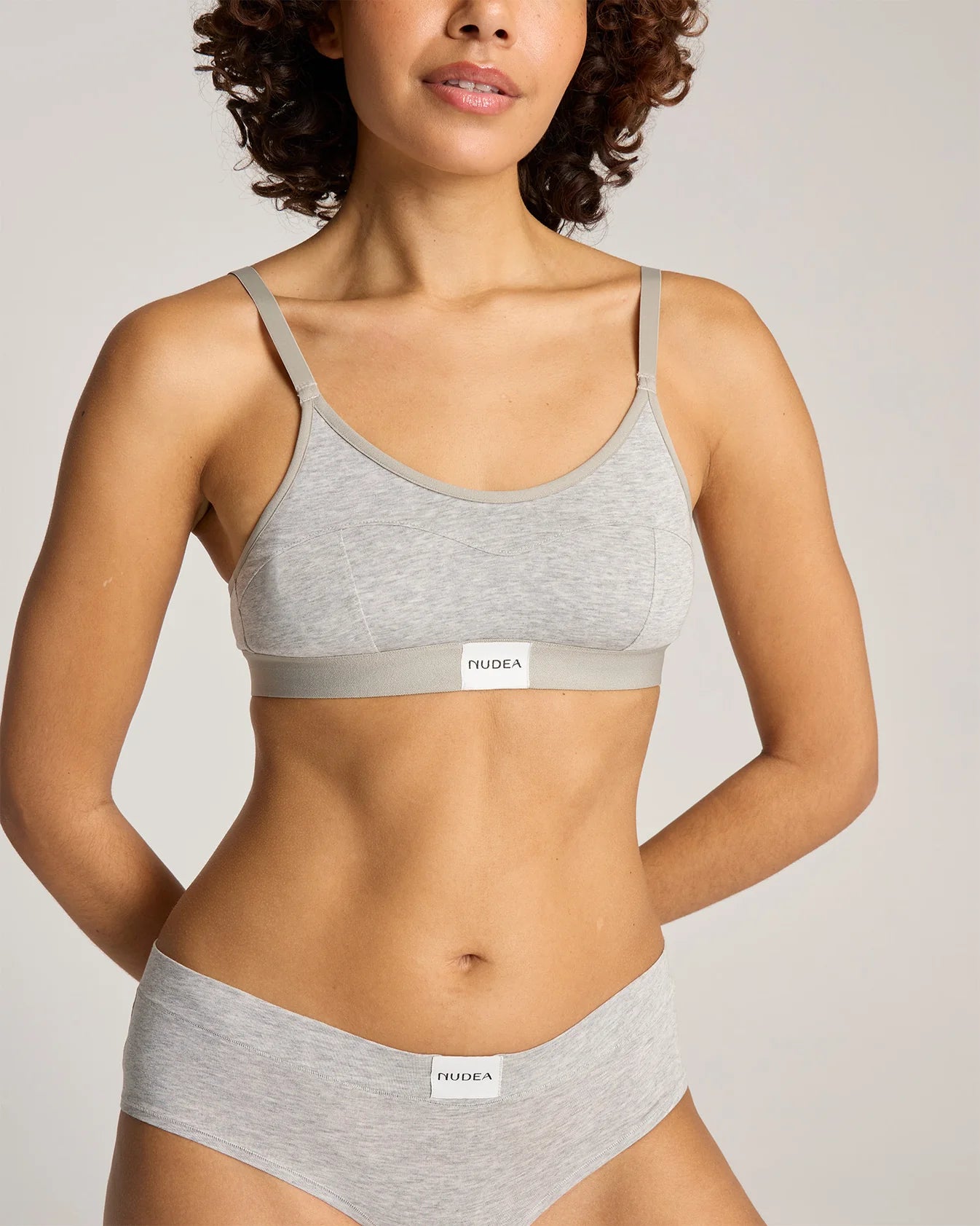 Woman wearing grey cotton bralette and briefs in front of a grey background
