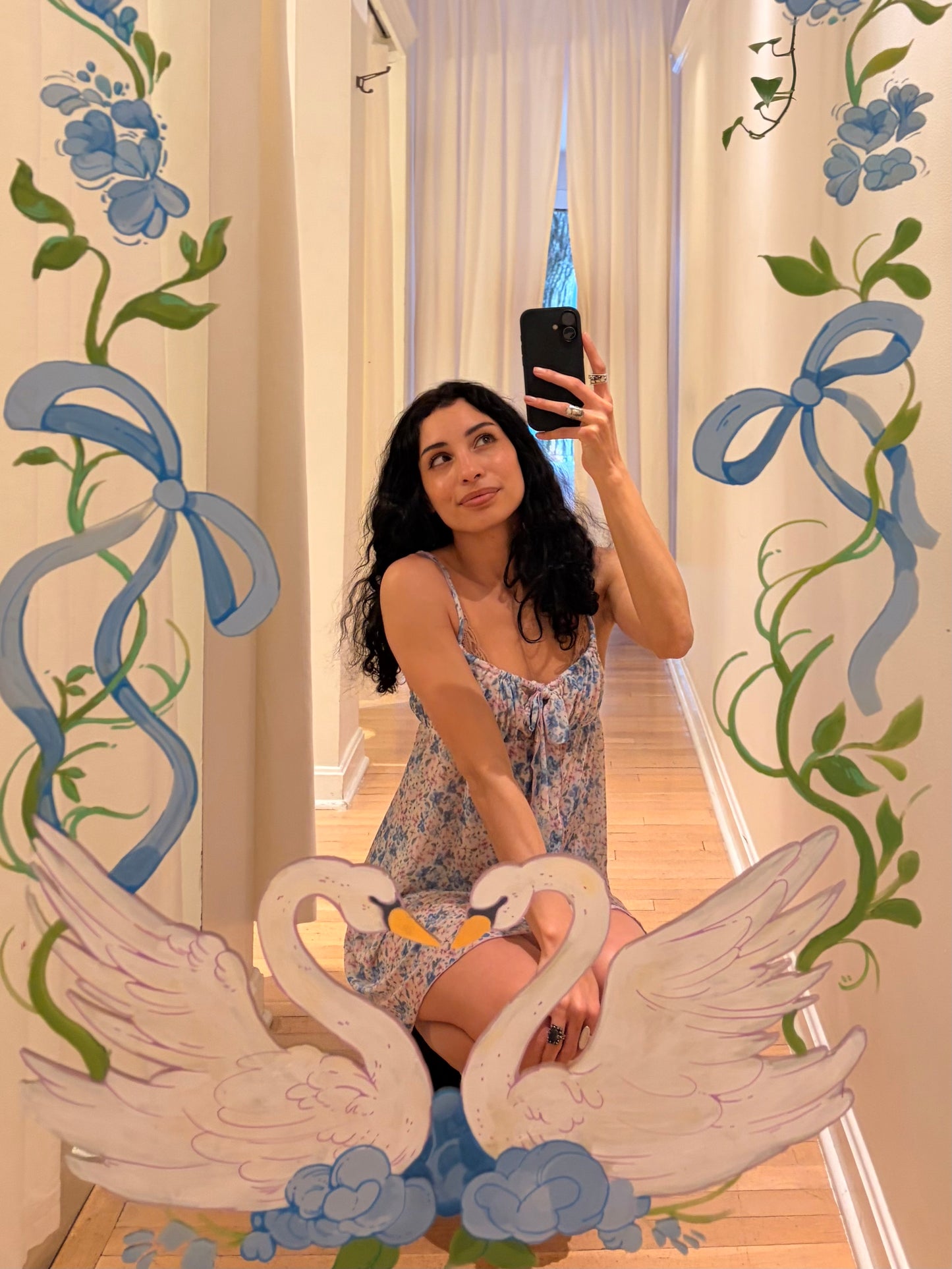Woman taking a mirror selfie in a room with decorative swan and floral elements.