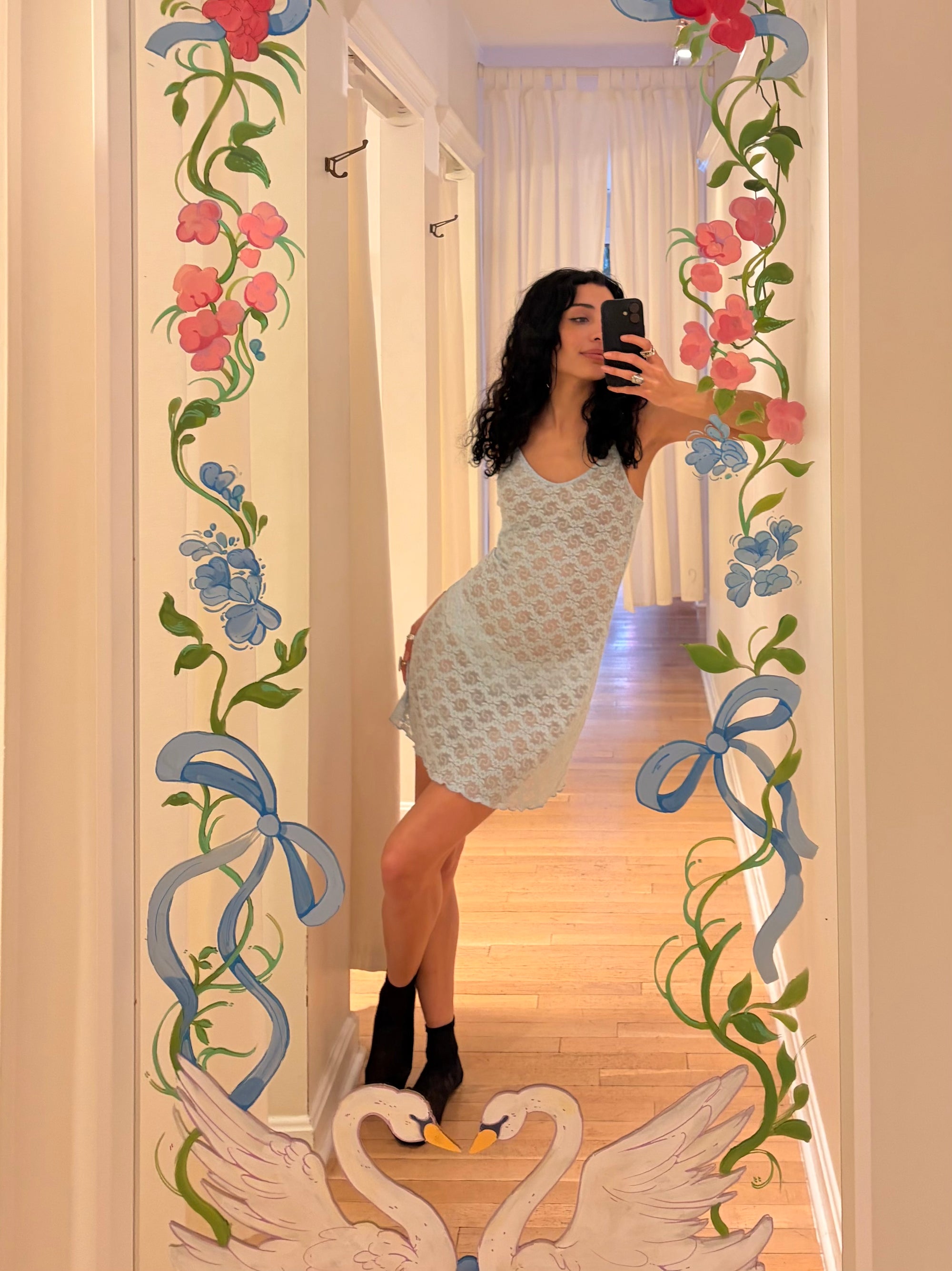 Person taking a mirror selfie with decorative floral and swan designs on the frame.
