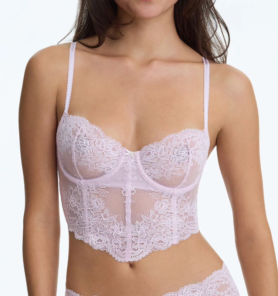 A close-up of a model wearing a light pink lace and mesh underwire bra with thin shoulder straps and a scalloped lace hem.