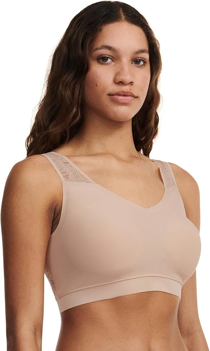 A woman wearing a light beige wireless bralette with lace trim on the straps, shown from the chest up against a plain white background.