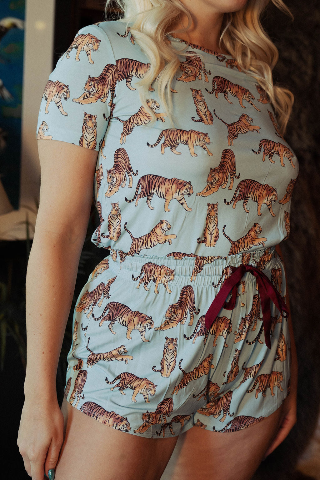 Model with blue short sleeve pajama set with orange tigers and a red drawstring on a dark background. 