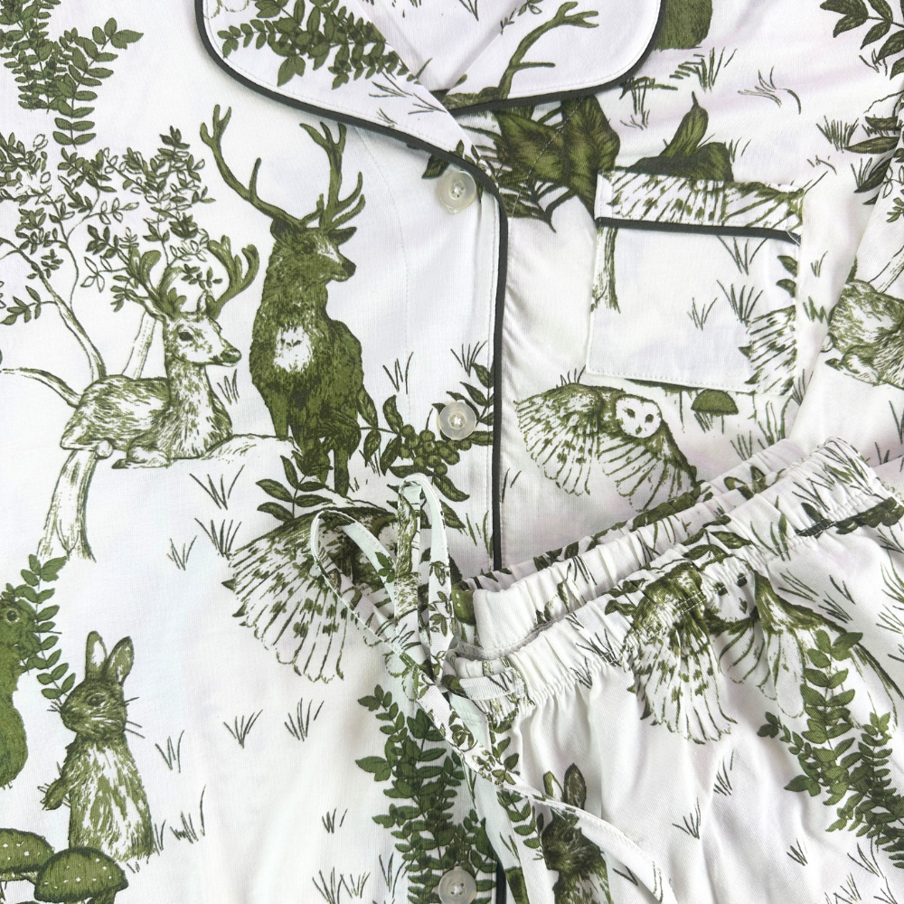 close of of white pajamas with owls, deer, bunny, mushroom and fern illustrations all over.