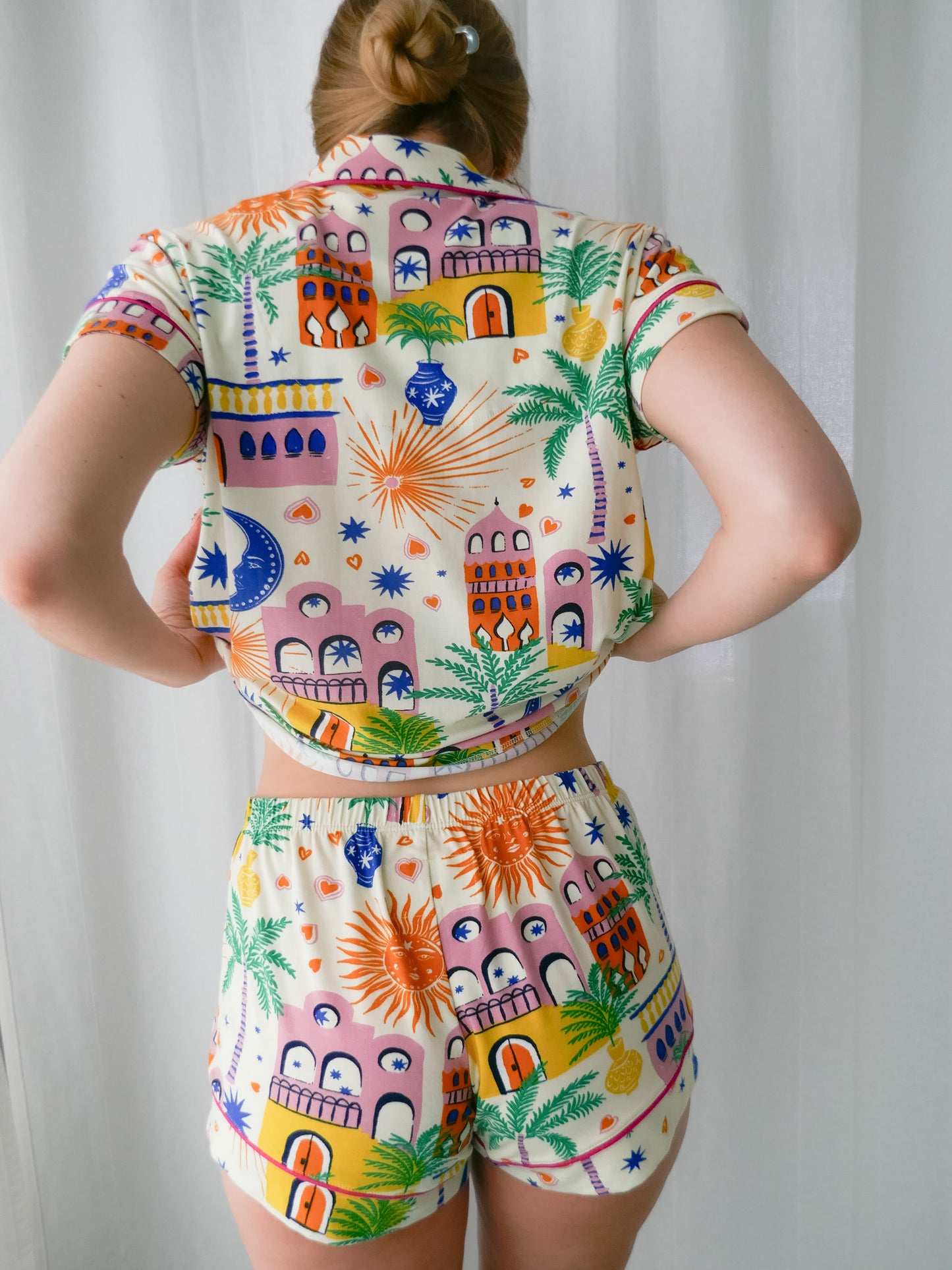 Person wearing a colorful outfit with a pattern of buildings and palm trees against a plain background