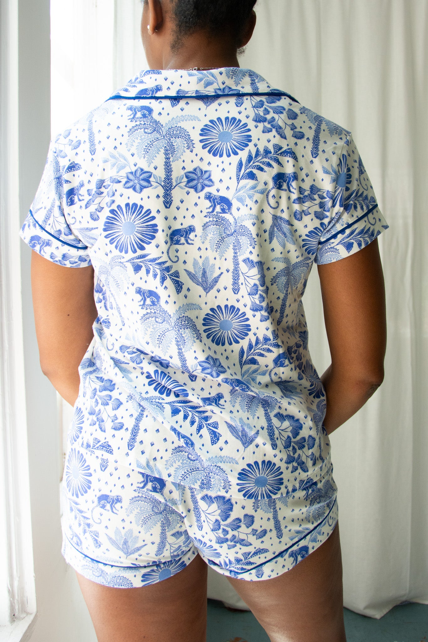 Person wearing a blue and white floral pajama set against a white curtain background