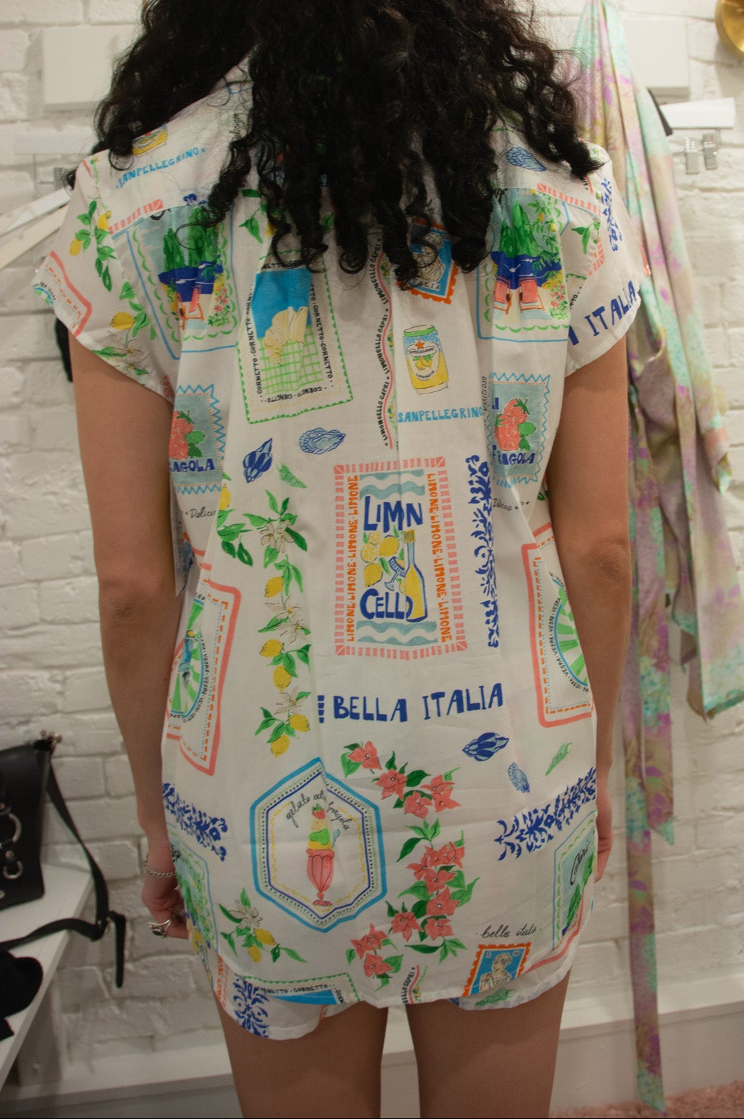 Person wearing a colorful embroidered pajamas in a room with a white brick wall.