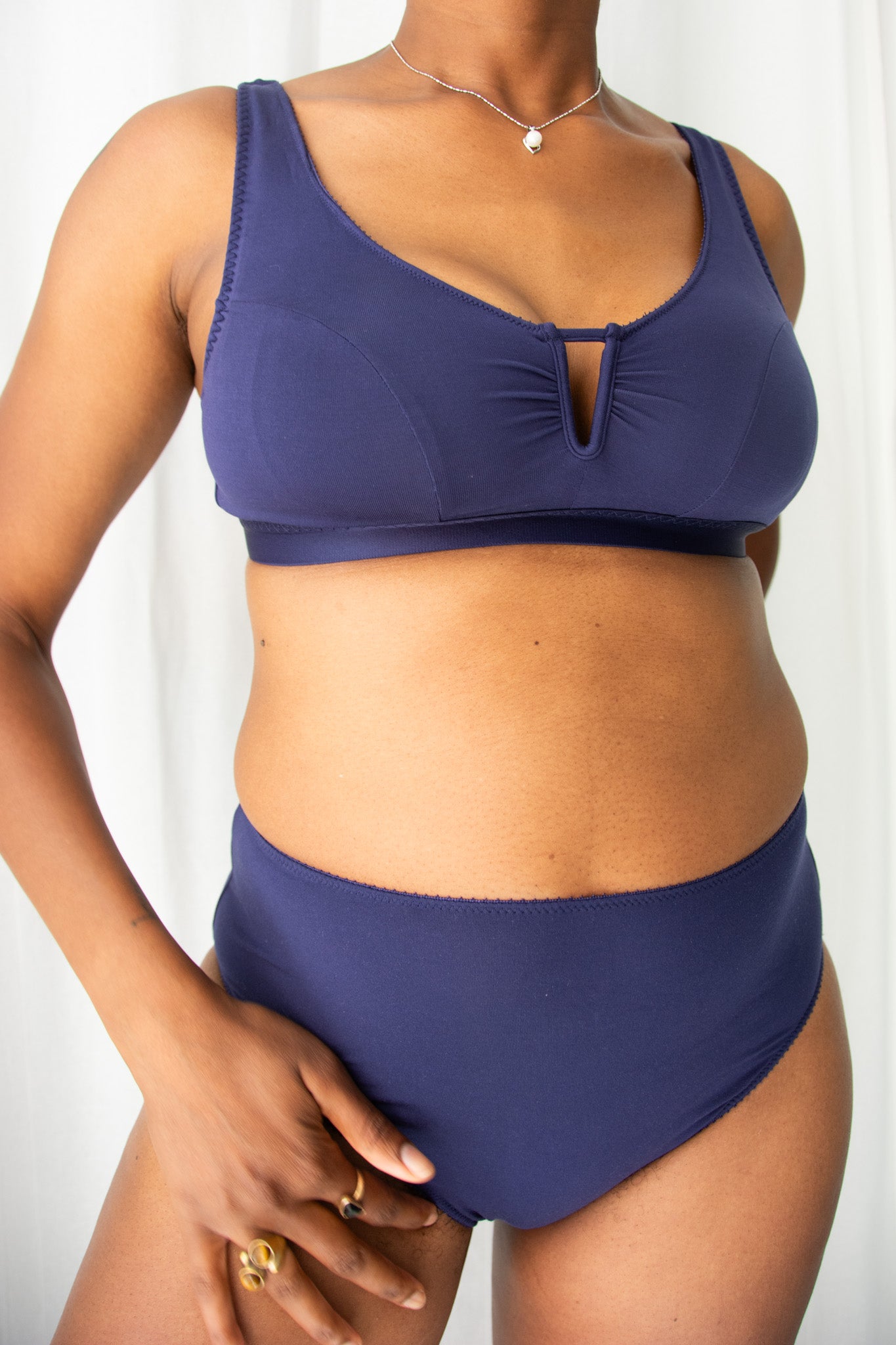 Woman wearing a navy bra and underwear against a white curtain background