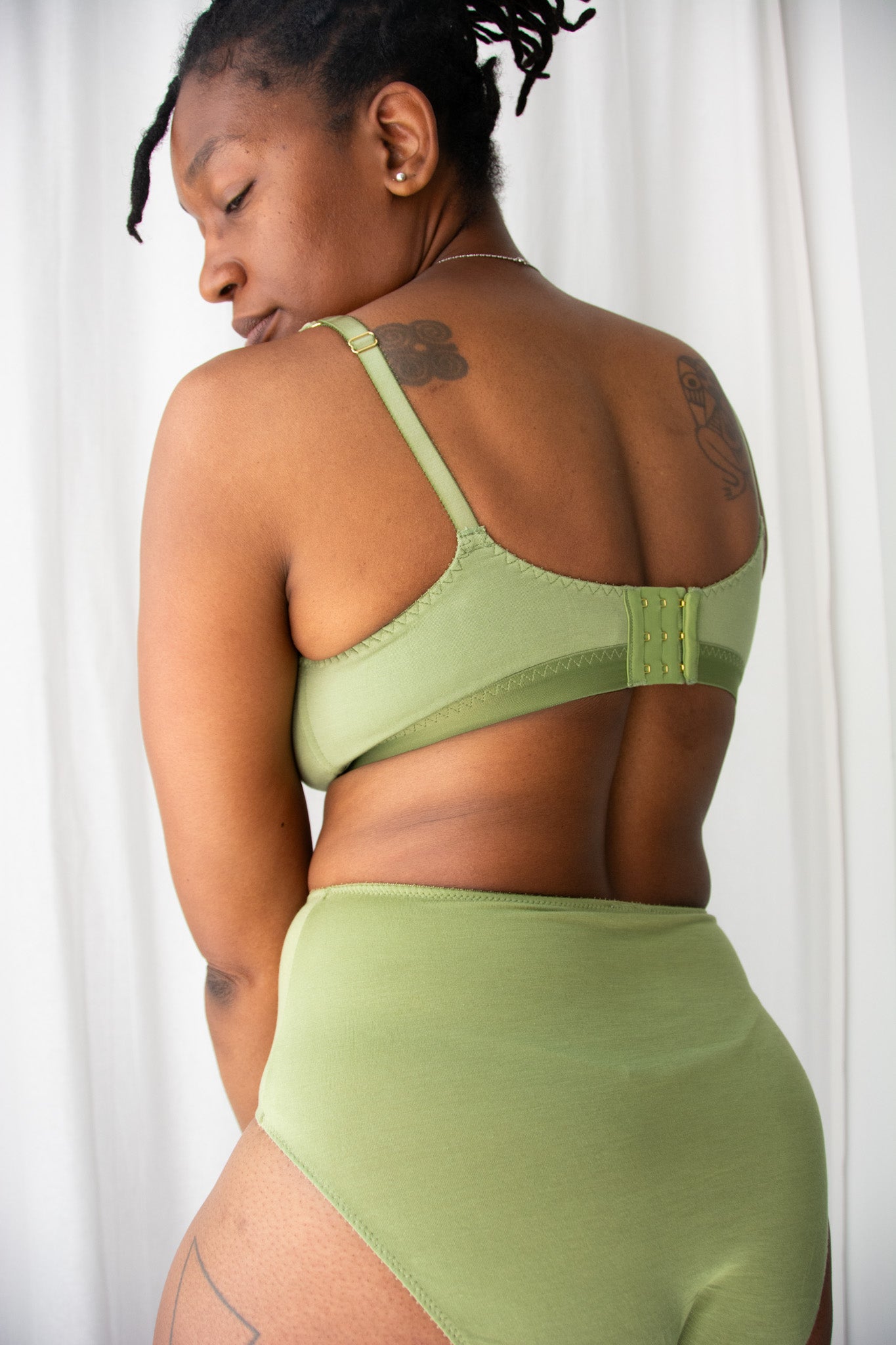 Person wearing a green sports bra and leggings set against a white curtain background