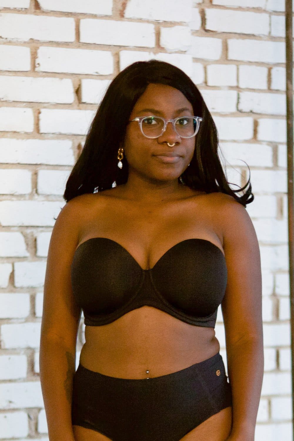 Wacoal red carpet strapless bra in black, front view on a model against a brick wall.