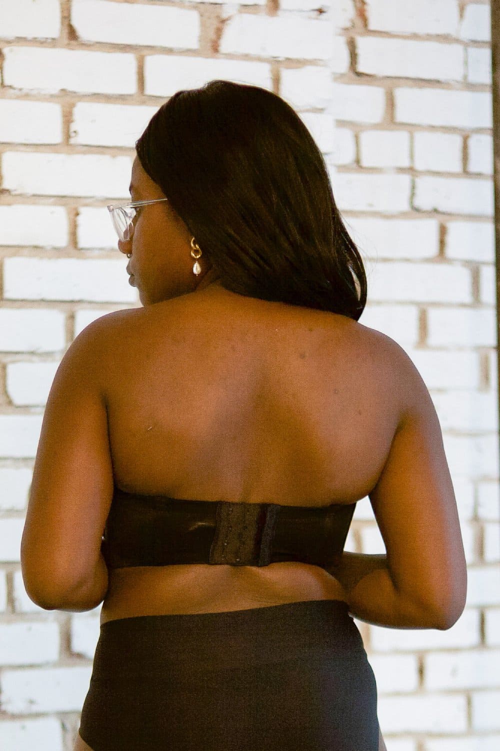 Wacoal red carpet strapless bra in black, back view on a model against a brick wall.