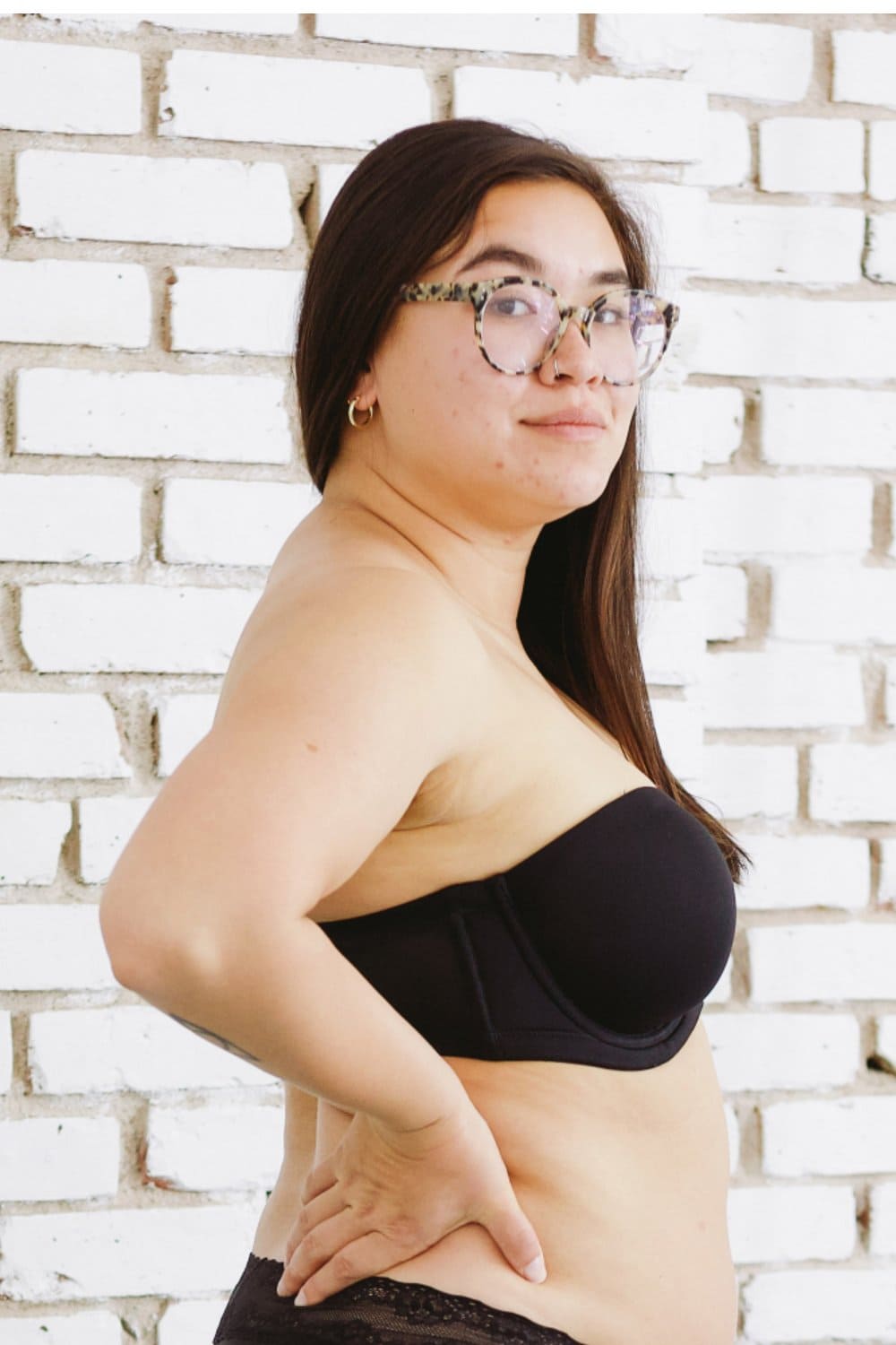 Wacoal red carpet strapless bra in black, front-side view on a model against a brick wall.