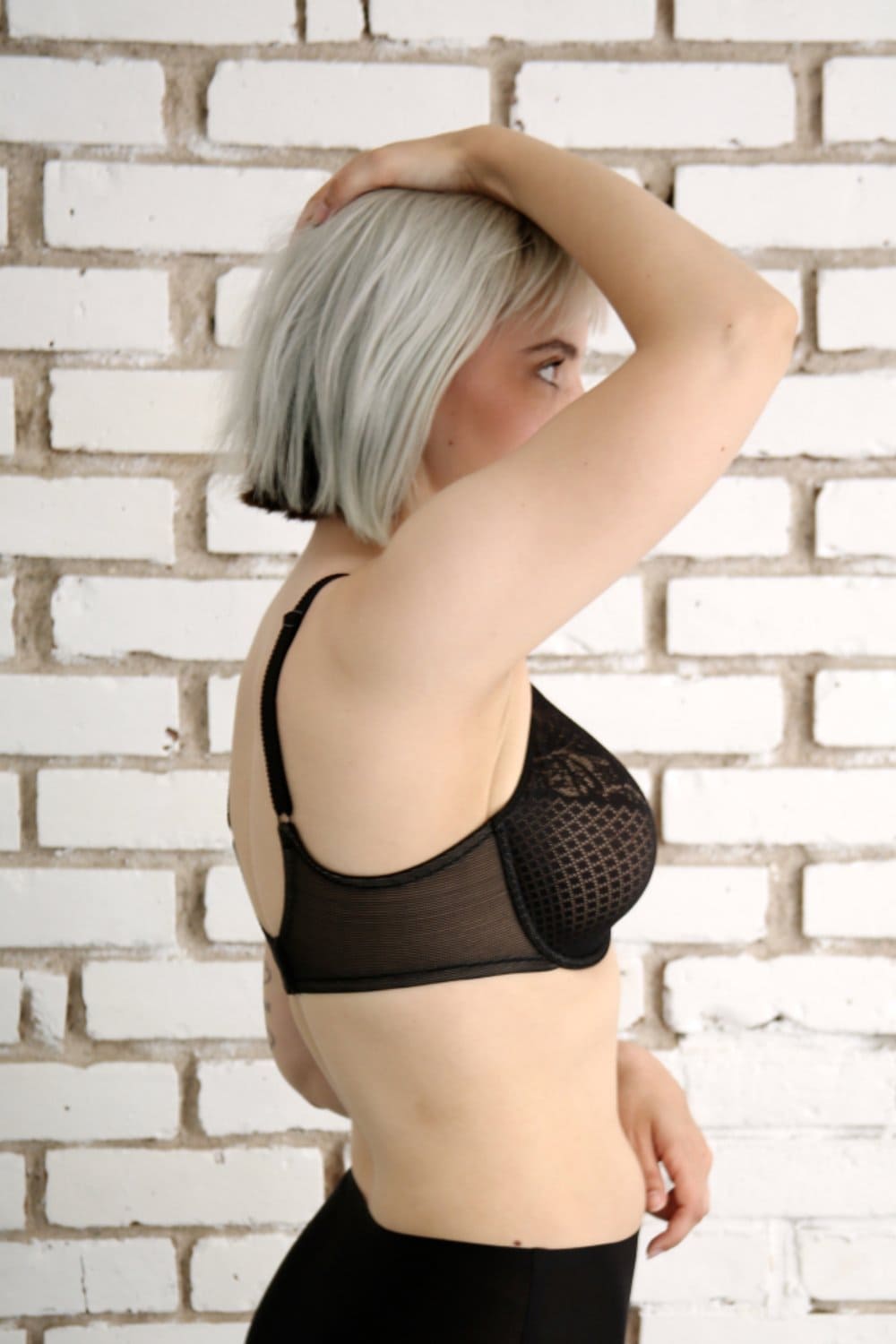 Wacoal Visual Effects Minimizer bra in black, side close-up on a model against a brick wall.