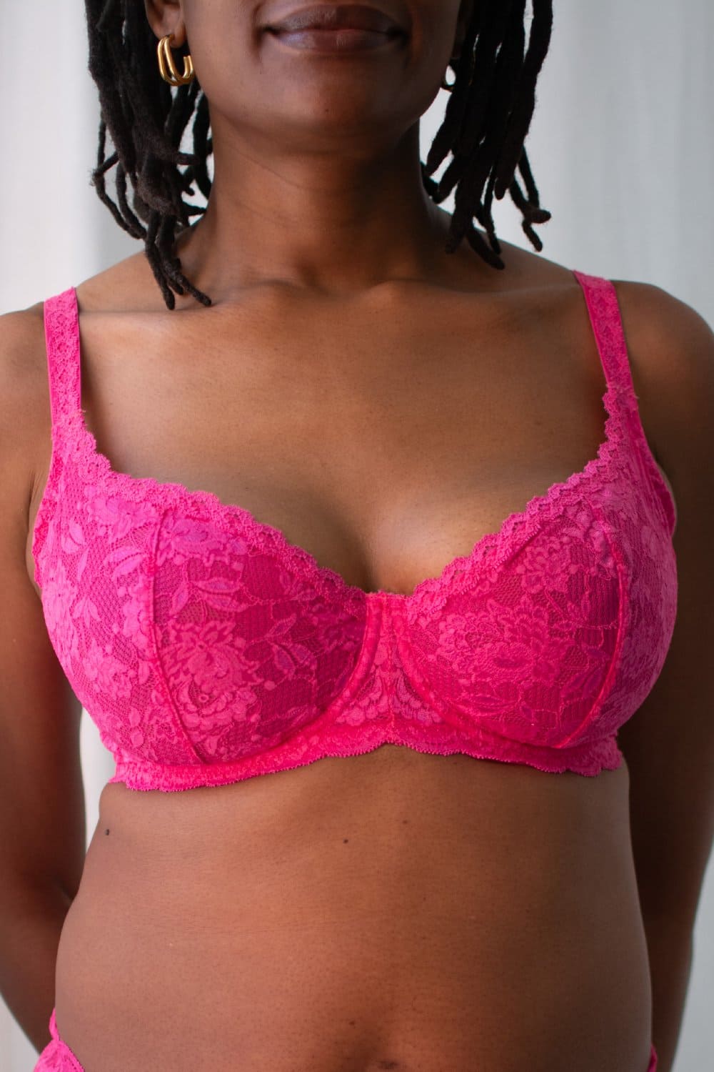 Person wearing a bright pink lace bra against a neutral background