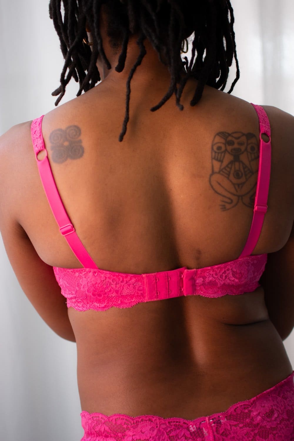 Person wearing a bright pink bra and underwear set with tattoos visible on the back.