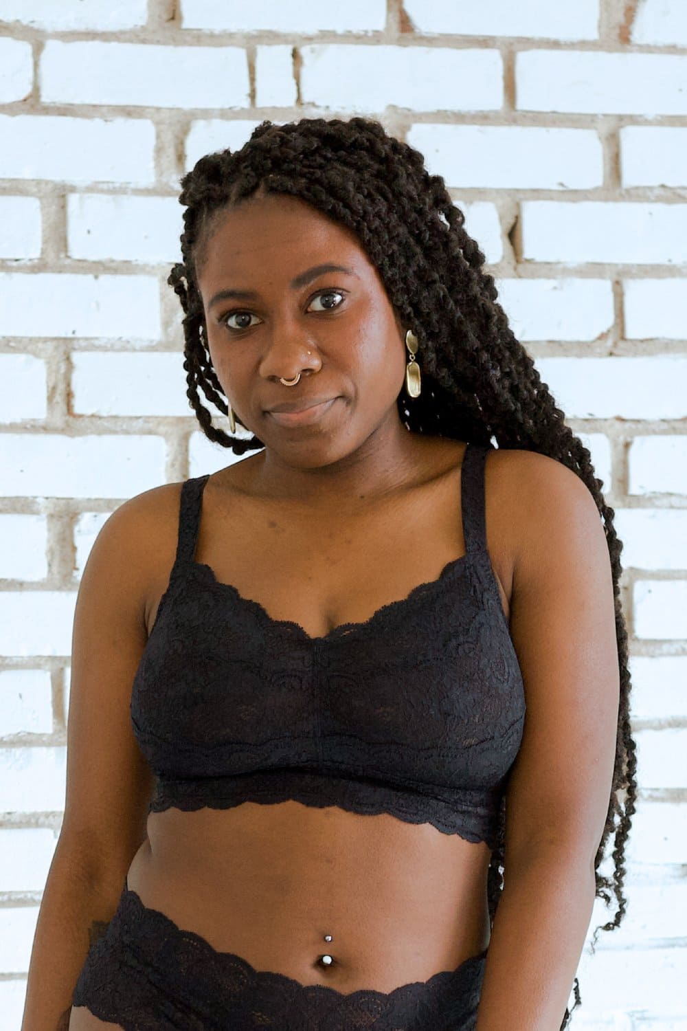 Person wearing black lingerie set against a white brick wall.