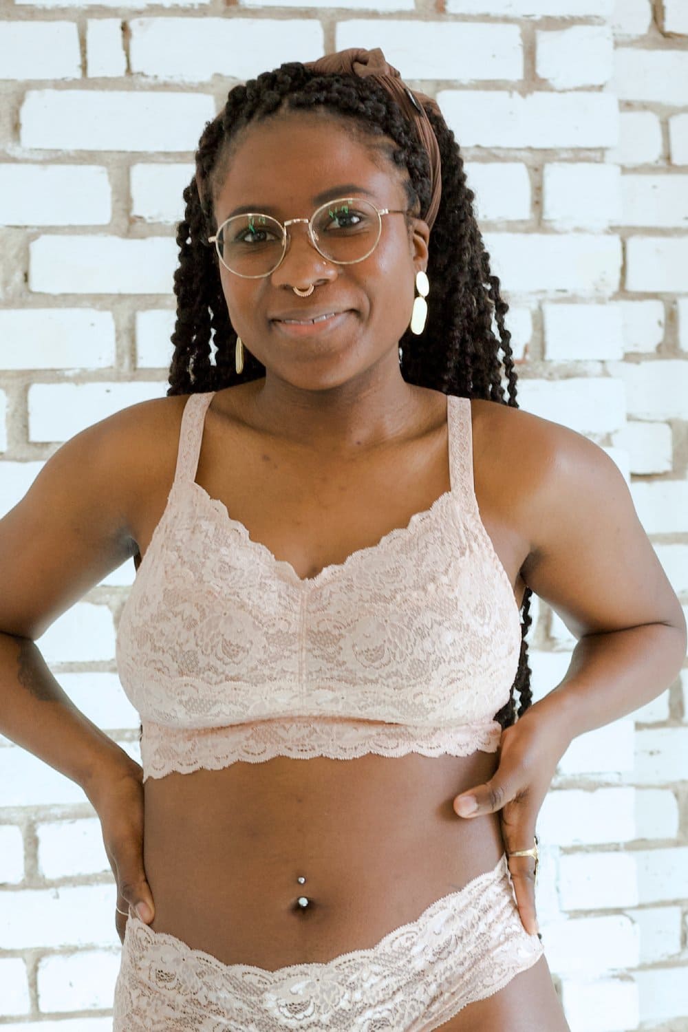 Person wearing beige lace lingerie set against a white brick wall