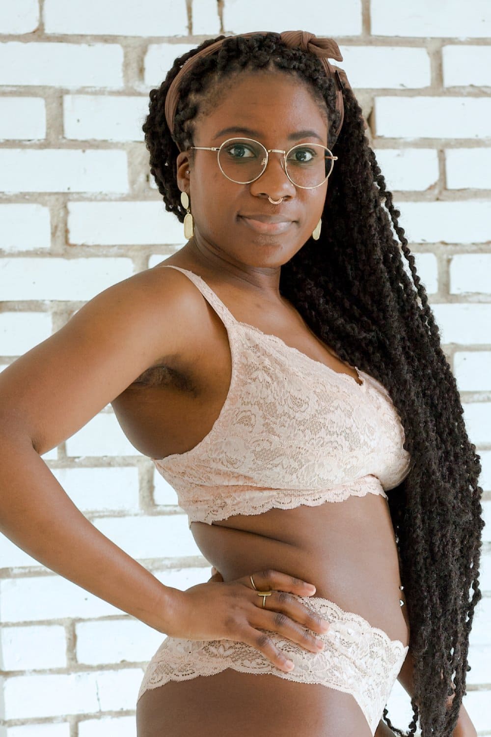 Person wearing beige lace lingerie set against a white brick wall