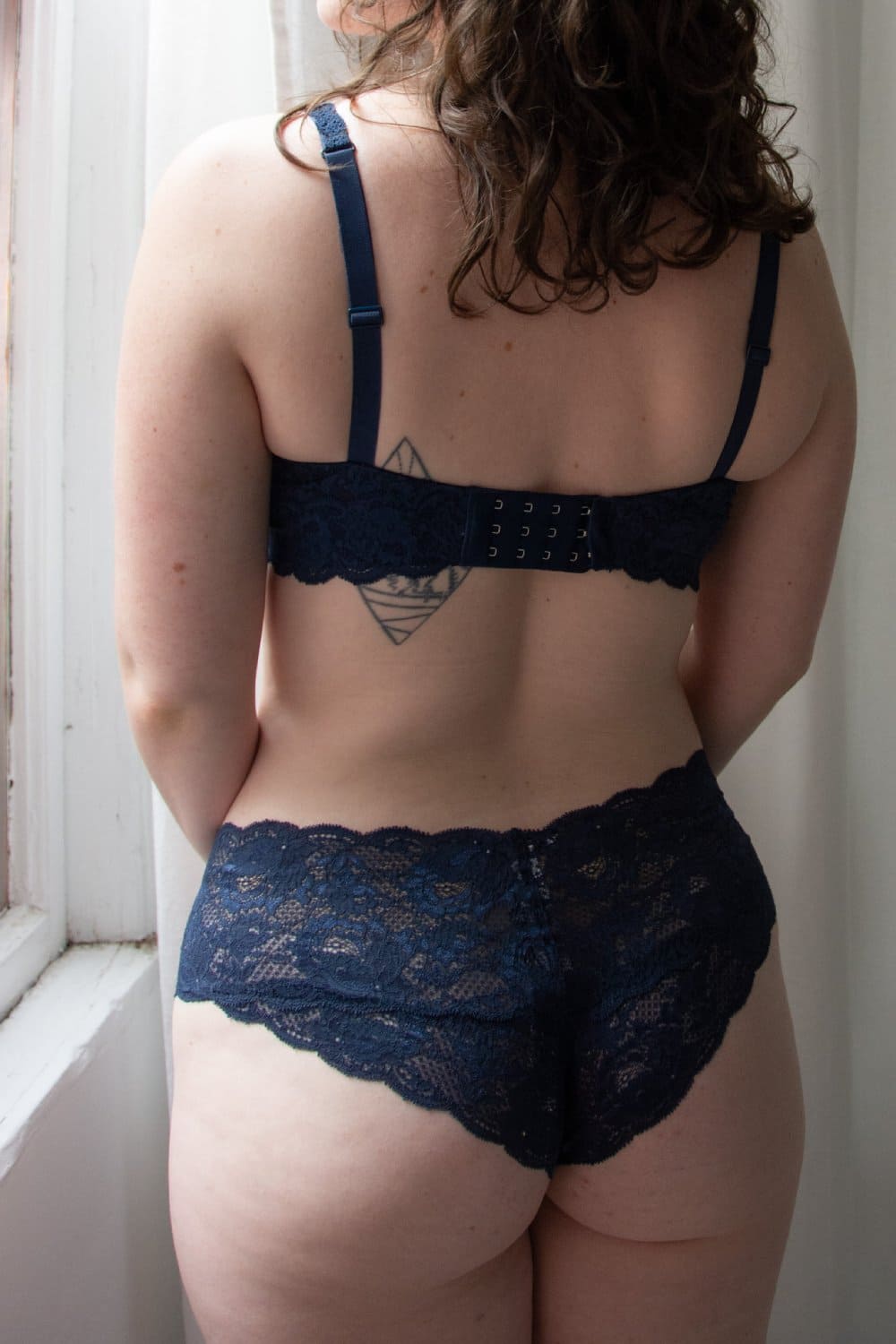 Person wearing a navy blue lace bra and panties set in a softly lit room.