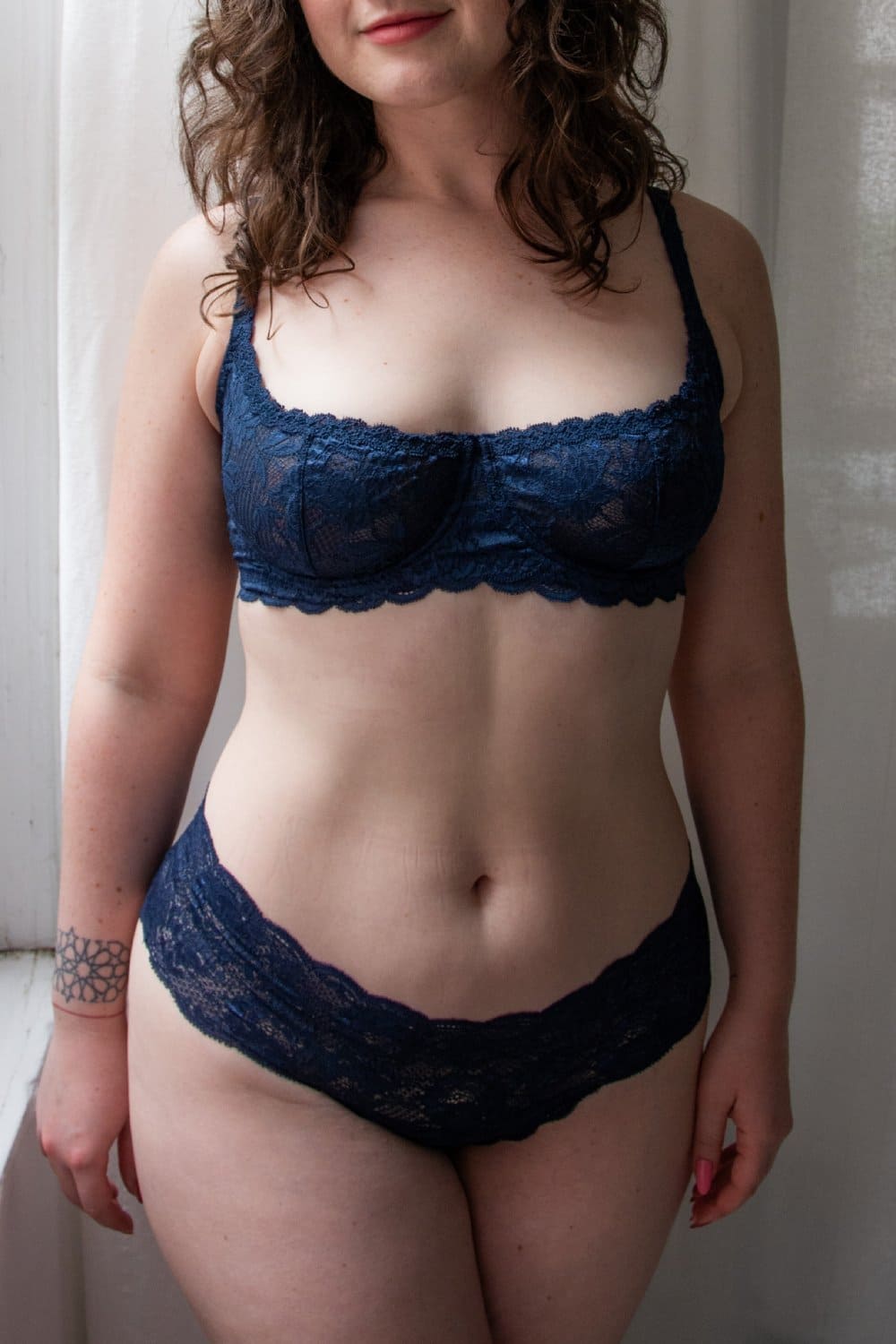 Woman wearing a navy blue lace bra and panties set against a neutral background.