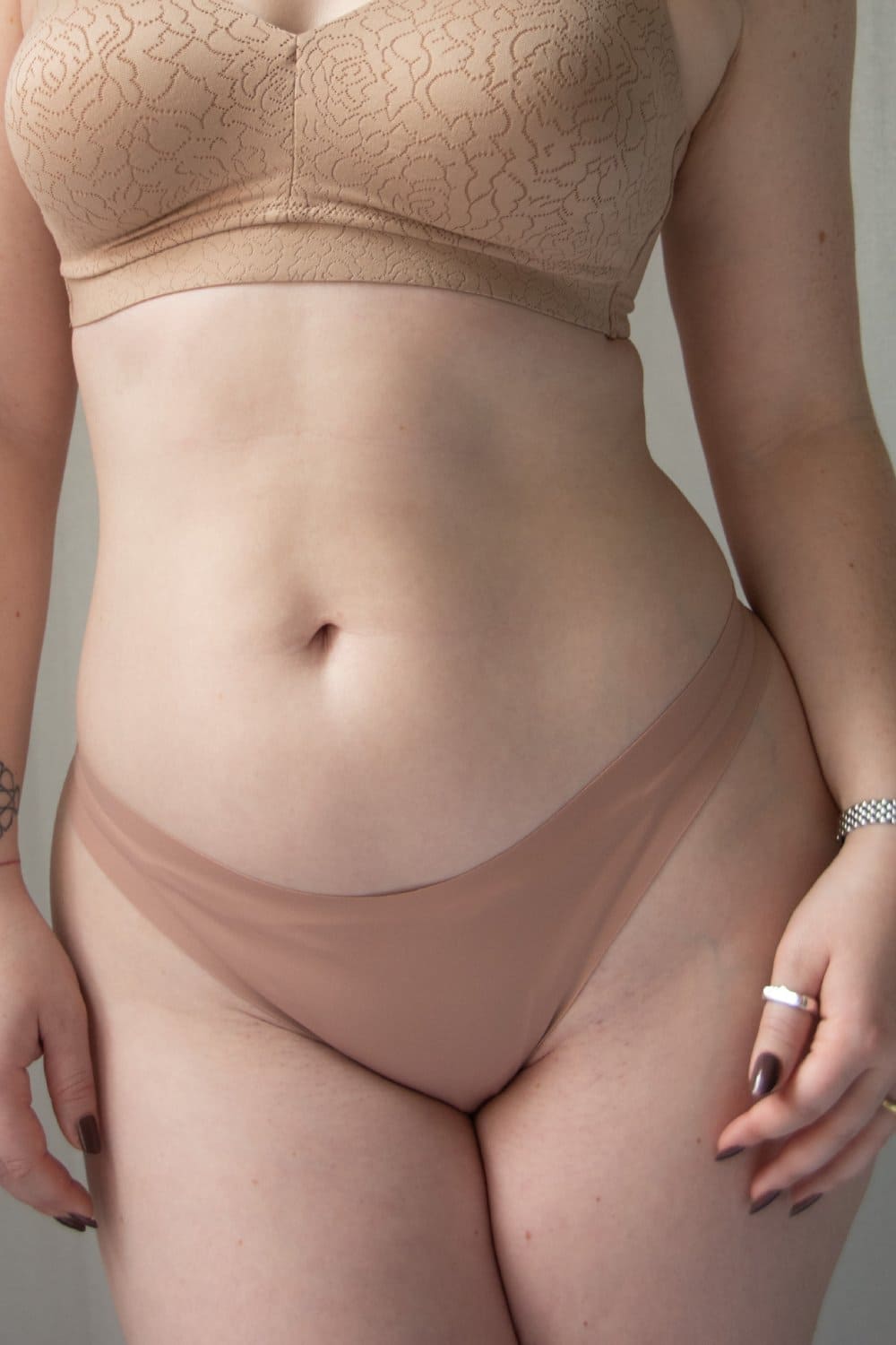 Fleur du mal le stretch micro thong in tan, front view on a model, close-up.